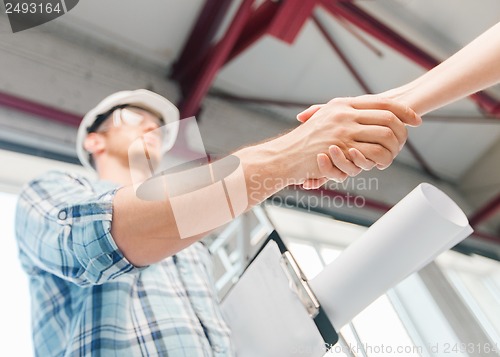 Image of builder with blueprint shaking partner hand