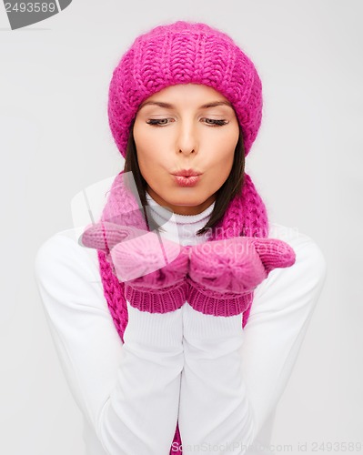 Image of happy woman in winter clothes blowing on palms