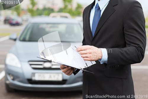 Image of man with car documents outside