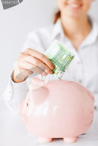 Image of woman puts euro cash into large piggy bank