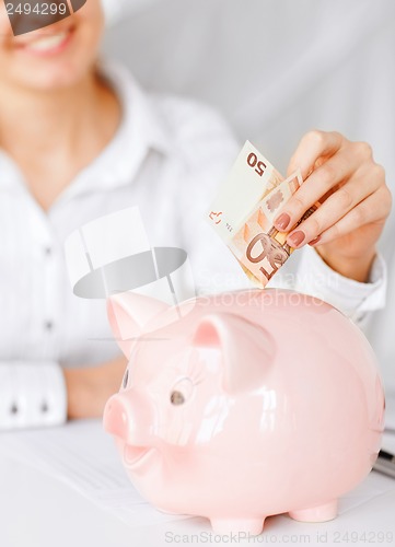 Image of woman puts euro cash into large piggy bank