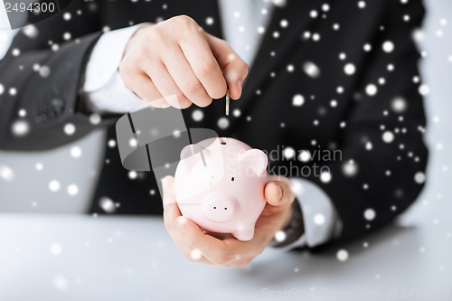 Image of man putting coin into small piggy bank