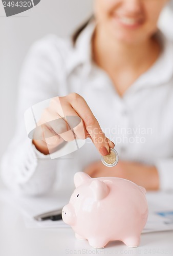 Image of woman hand putting coin into small piggy bank