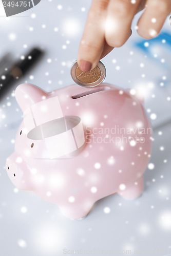 Image of woman hand putting coin into small piggy ban