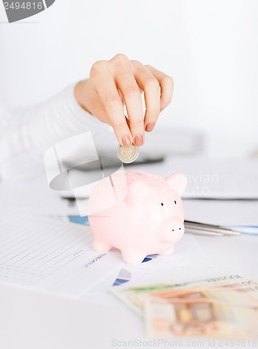 Image of woman hand putting coin into small piggy bank