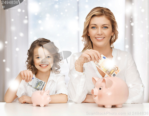 Image of mother and daughter with piggy banks and money