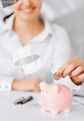 Image of woman hand putting coin into small piggy bank