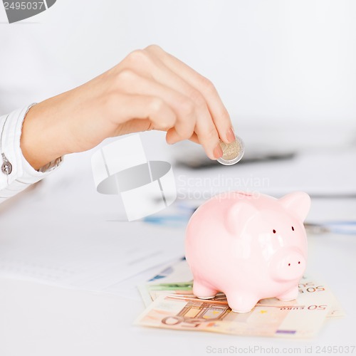 Image of woman hand putting coin into small piggy bank