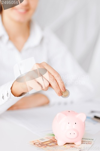 Image of woman hand putting coin into small piggy bank