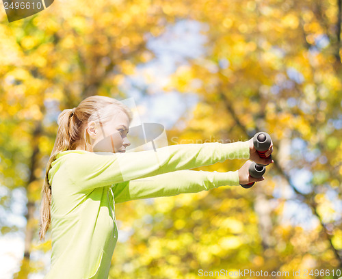 Image of sporty woman with light dumbbells outdoors