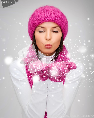 Image of happy woman in winter clothes blowing on palms