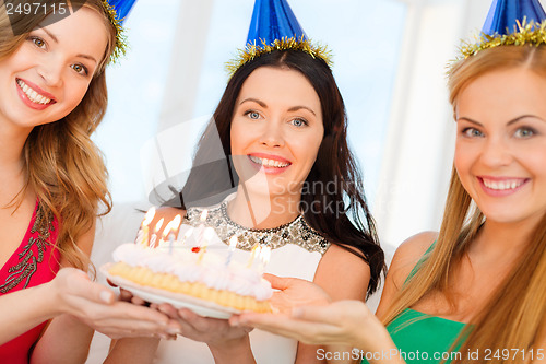 Image of three women wearing hats holding cake with candles