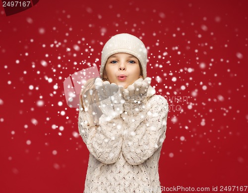 Image of happy girl in winter clothes blowing on palms