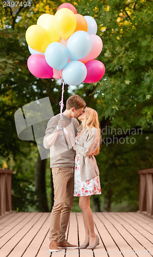 Image of couple with colorful balloons kissing in the park