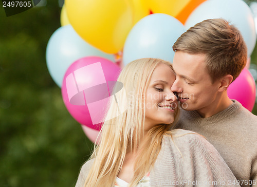 Image of couple with colorful balloons kissing in the park