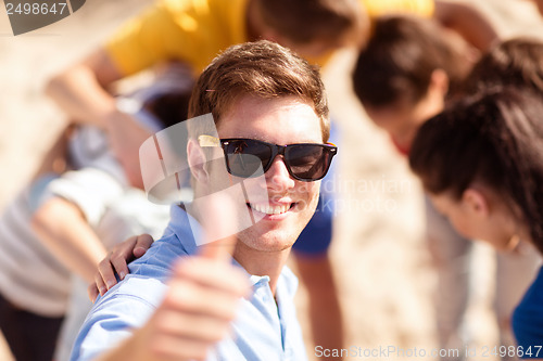 Image of man with friends on the beach showing thumbs up