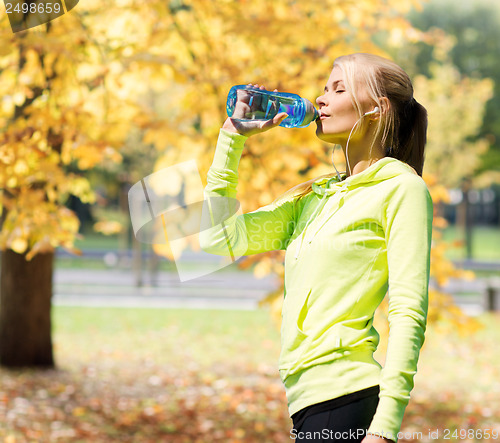 Image of woman drinking water after doing sports outdoors