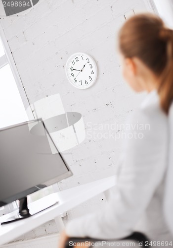 Image of businesswoman looking at wall clock in office