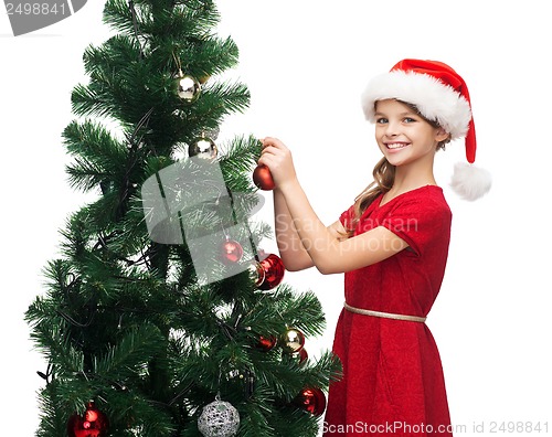 Image of smiling girl in santa helper hat decorating a tree