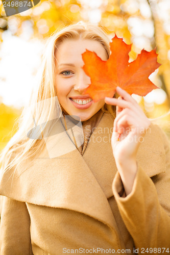 Image of woman with red marple leaf in the autumn park