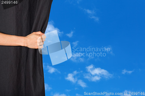 Image of Hand opening a curtain with blue sky behind it