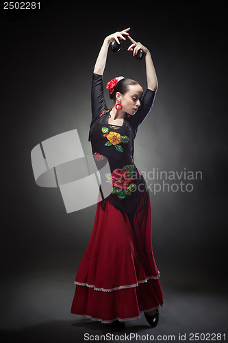 Image of young woman dancing flamenco with castanets on black