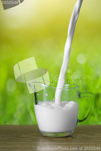 Image of Milk pouring into the glass on nature background