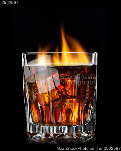 Image of cola with cognac and fire in glass on black