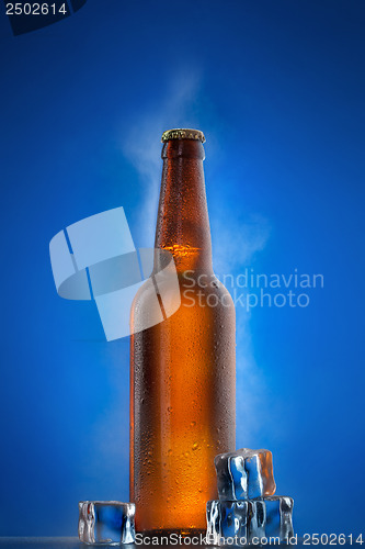 Image of Cold beer bottle with drops, frost and vapour on blue