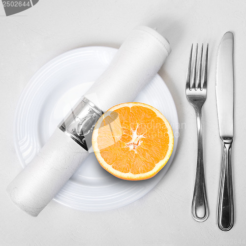 Image of fresh orange on plate served with knife, fork and napkin