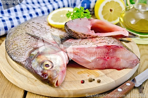 Image of Bream raw on a round board with a knife and oil