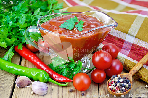 Image of Ketchup in a glass gravy boat with vegetables on the board
