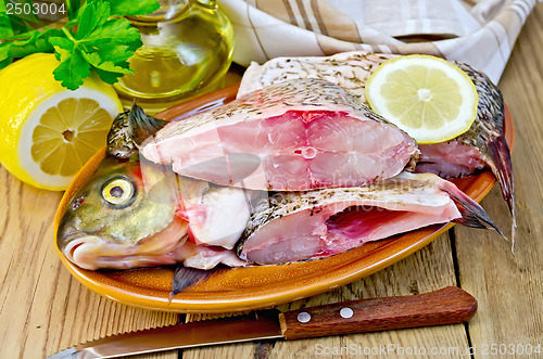 Image of Bream raw in a clay plate with a lemon on the board