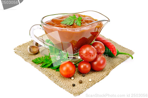Image of Ketchup in a glass gravy boat with vegetables on sacking