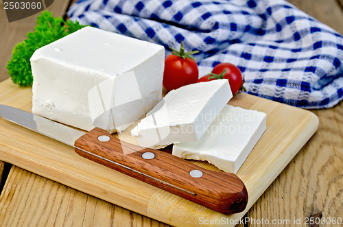 Image of Feta cheese on a board with a knife and tomato