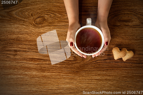 Image of woman holding hot cup of tea with cookies on wooden table