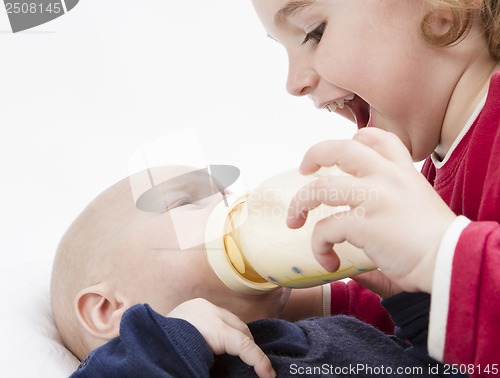 Image of young child feeding toddler with milk bottle