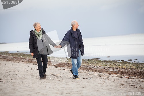 Image of mature happy couple walking on beach in autumn