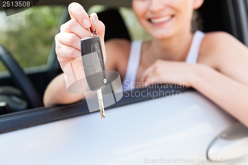 Image of young smiling woman sitting in car taking key 