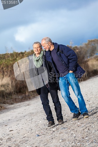 Image of mature senior couple walking on the beach autumn winter