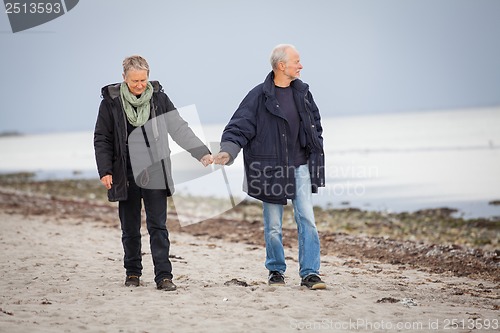 Image of mature happy couple walking on beach in autumn