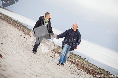 Image of mature happy couple walking on beach in autumn