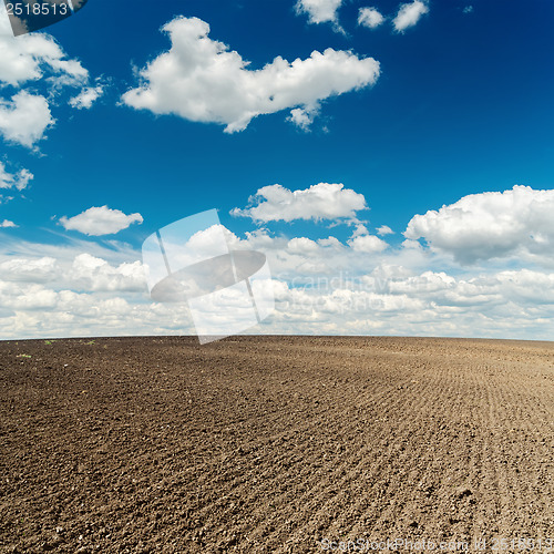 Image of plowed field and deep blue sky with clouds over it