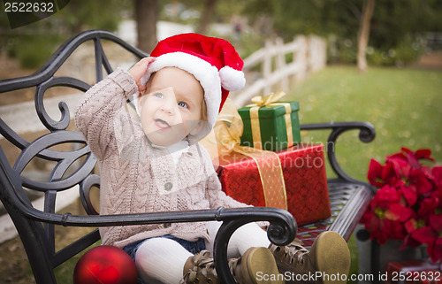 Image of Young Child Wearing Santa Hat Sitting with Christmas Gifts Outsi