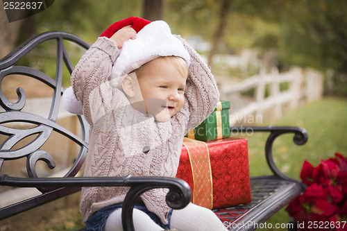 Image of Young Child Wearing Santa Hat Sitting with Christmas Gifts Outsi