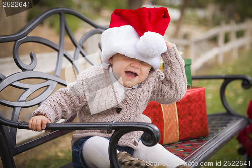 Image of Young Child Wearing Santa Hat Sitting with Christmas Gifts Outsi