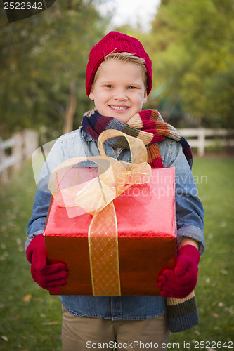 Image of Young Boy Wearing Holiday Clothing Holding Christmas Gift Outsid