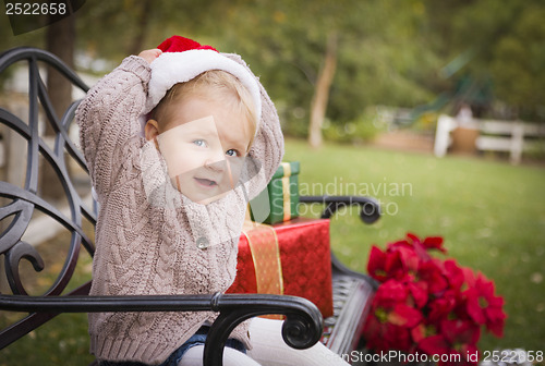 Image of Young Child Wearing Santa Hat Sitting with Christmas Gifts Outsi