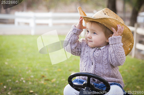 Image of Toddler Wearing Cowboy Hat and Playing on Toy Tractor Outside