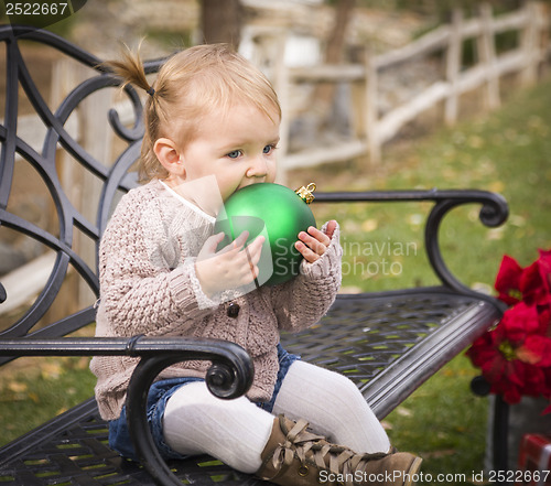 Image of Toddler Child Sitting on Bench with Christmas Ornament Outside